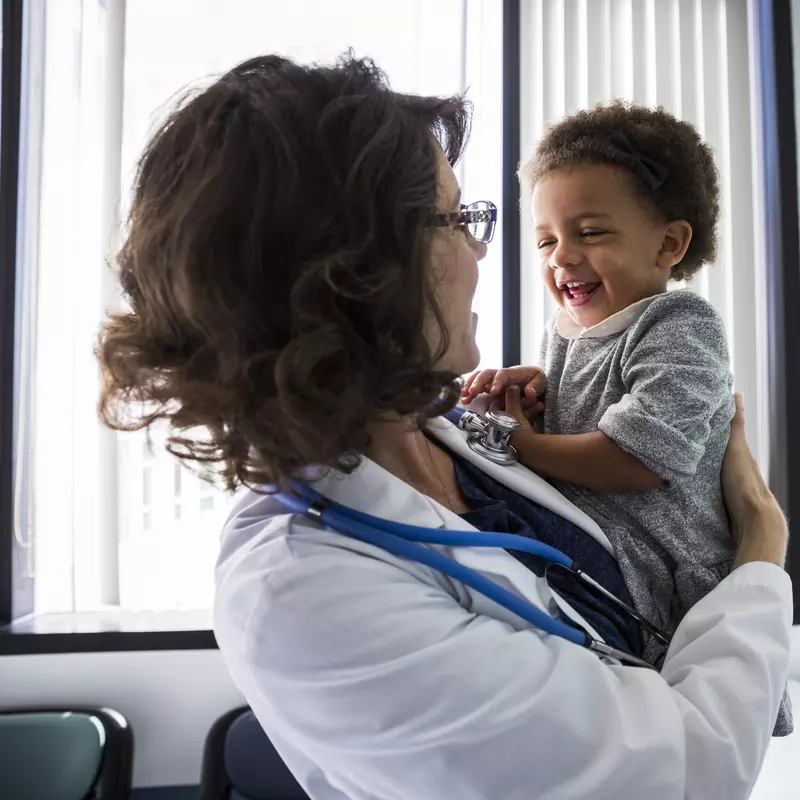 A female pediatrician holds a smiling infant in an exam room at AdventHealth.