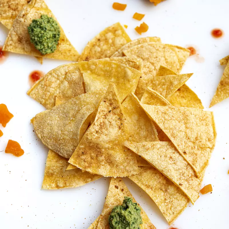 Pile of tortilla chips with salsa and guac.