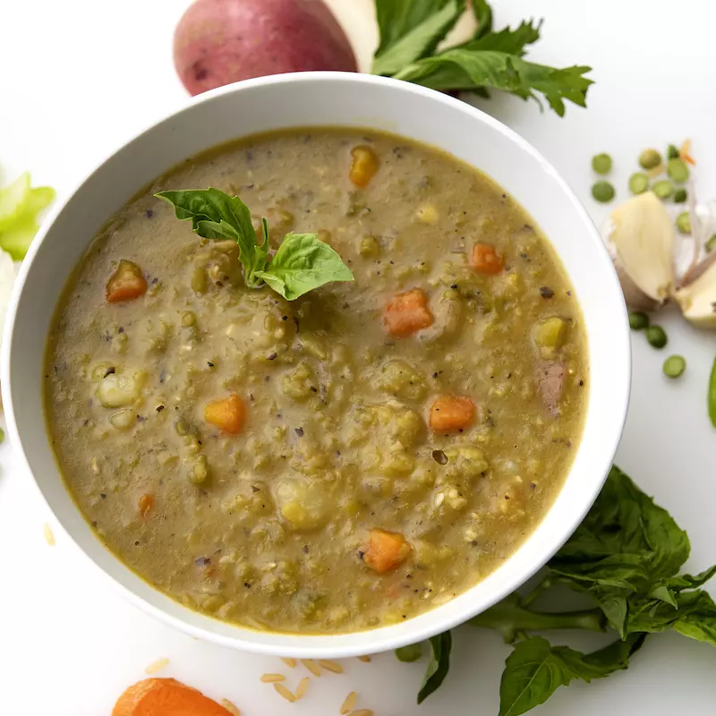 Bowl of split pea soup with onion and green garnishes