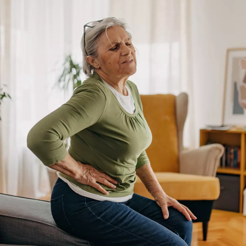 An older woman, sitting at home, holding her side in pain.