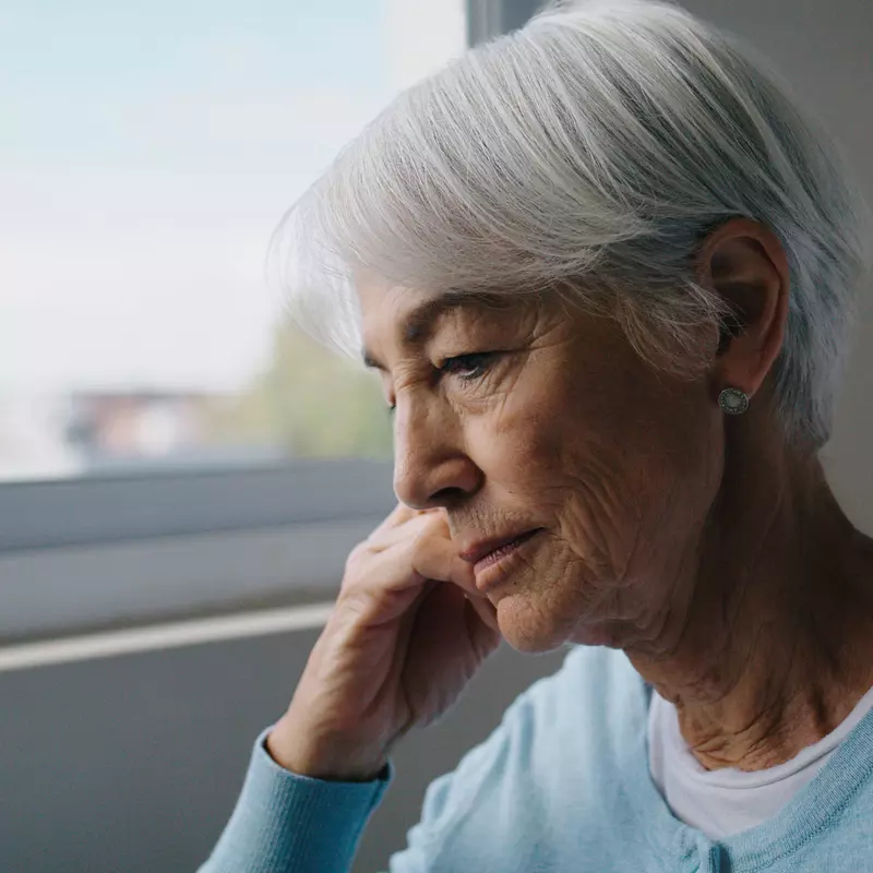 Older woman looking contemplative by a window indoors.