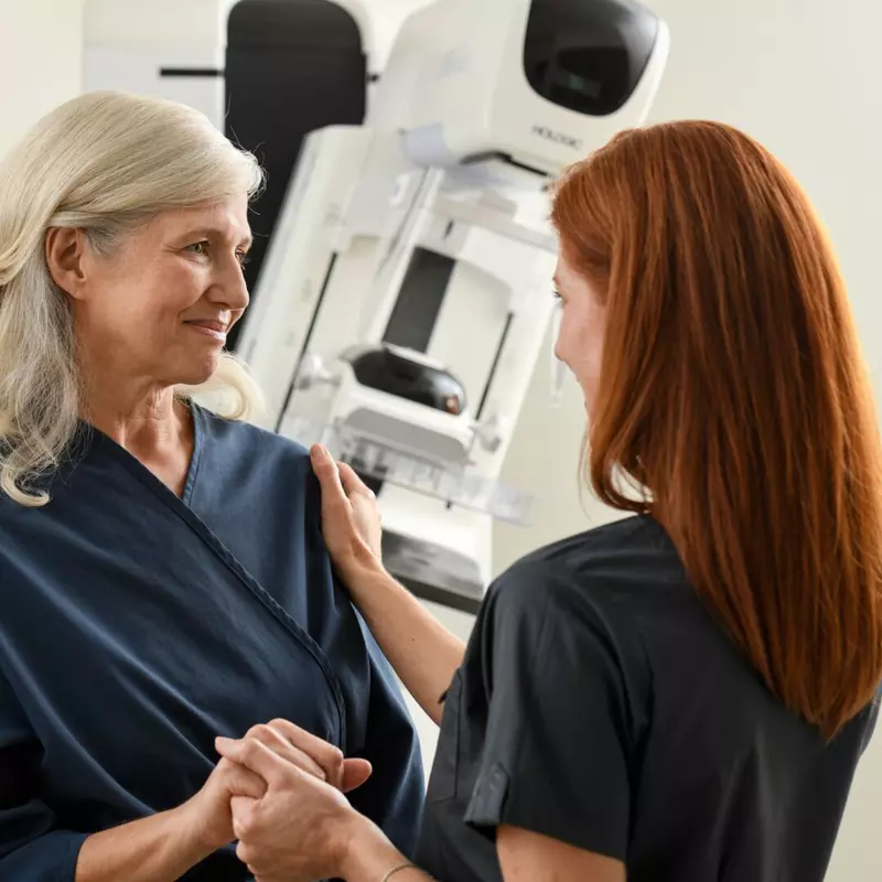 Woman with a technician before a mammogram standing in front of a mammography machine.