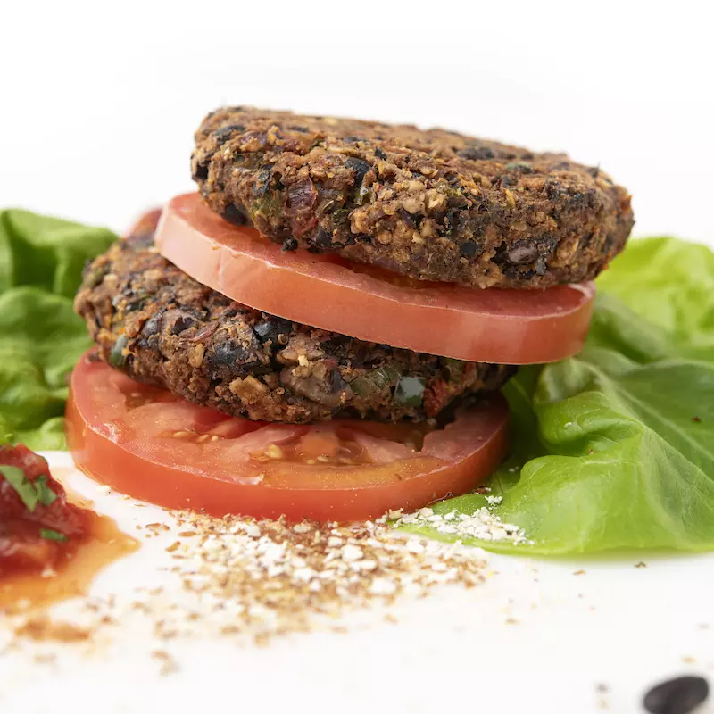 Two stacked bean burgers patties, sliced tomatoes, and lettuce leaves
