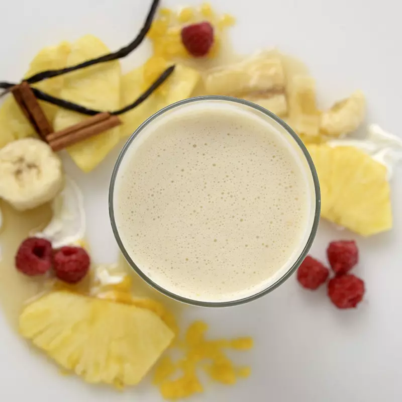 a creamy smoothie in a glass, surrounded by slices of pineapple and banana with vanilla bean pods