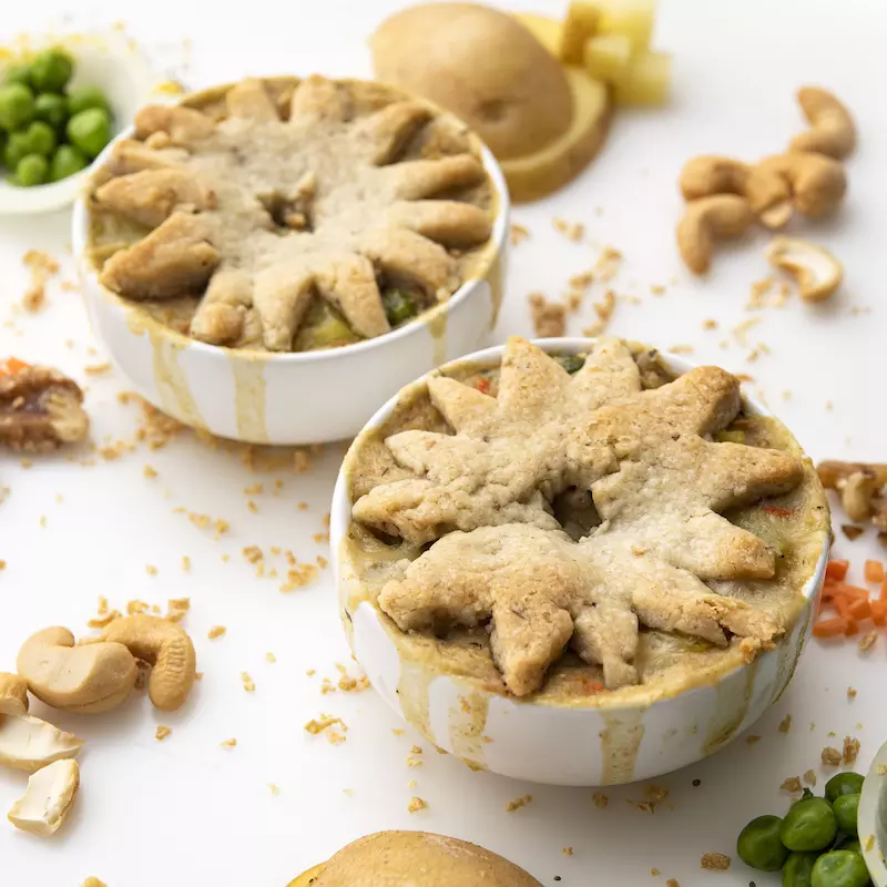 Two ramekins of pot pie on white surface with pea and cashew garnishes 