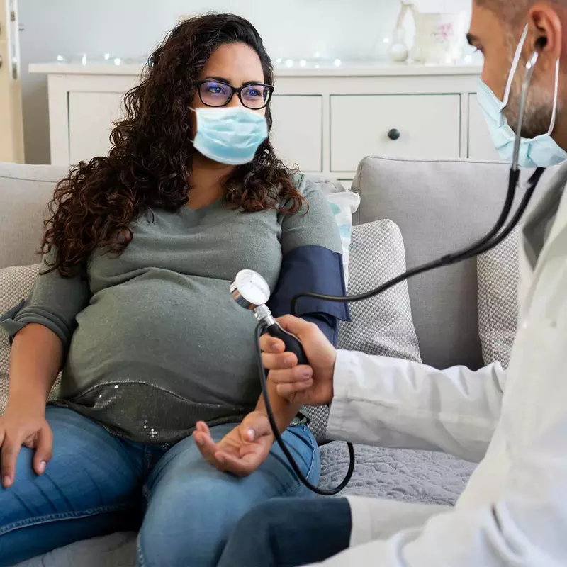 A pregnant woman has a check up while wearing a mask.