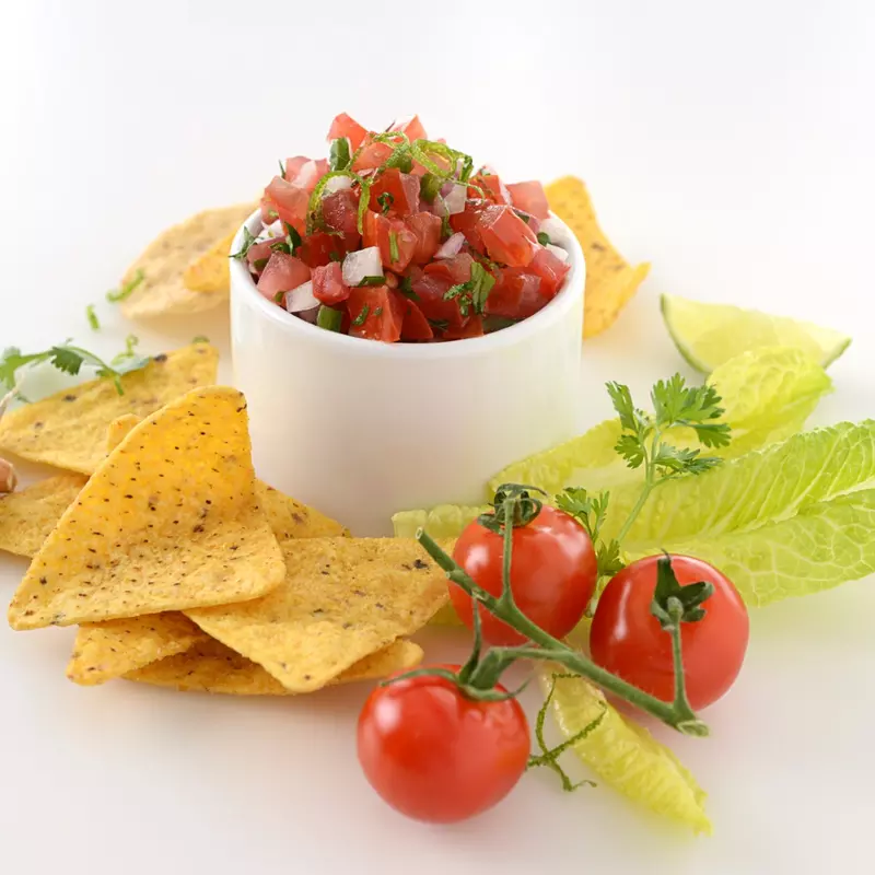 Dish of rustic tomato salsa surrounded by chips, garlic and tomatoes