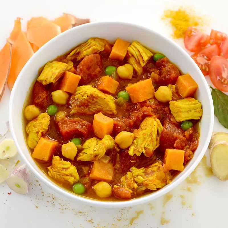 Dish of sweet potato and chicken curry surrounded by chopped potatoes and veggies