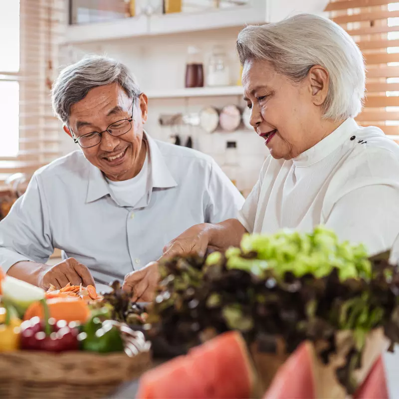 Senior couple sitting at the kitchen counter with produce on the kitchen table.