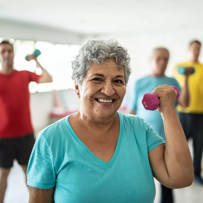 Senior woman smiling and lifting a free weight while in a group exercise class.