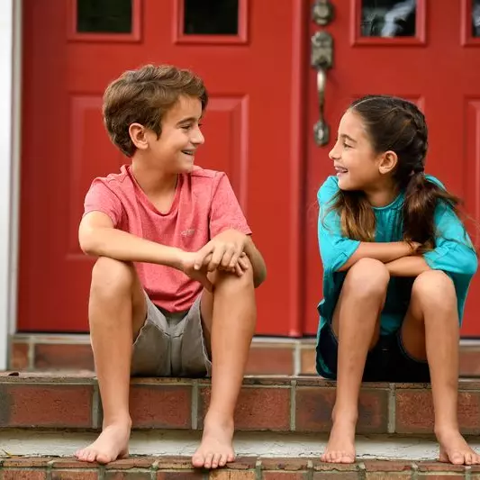 A boy and girl make jokes while sitting on their porch