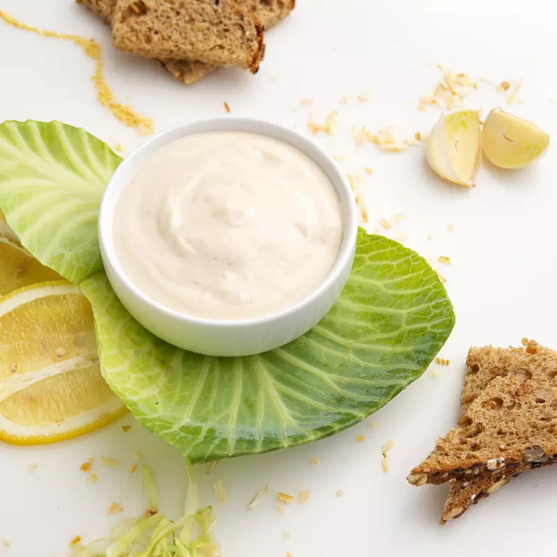 a small bowl filled with homemade mayonaise, surrounded by lettuce, lemons and crackers.