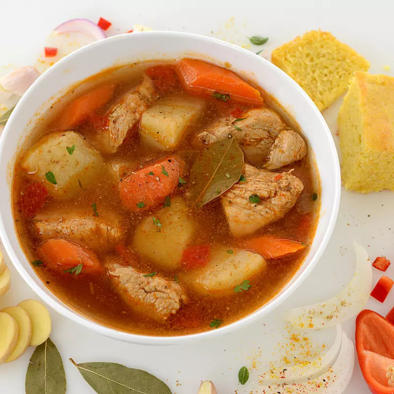 Bowl of chicken fricassee with cornbread and vegetable garnishes