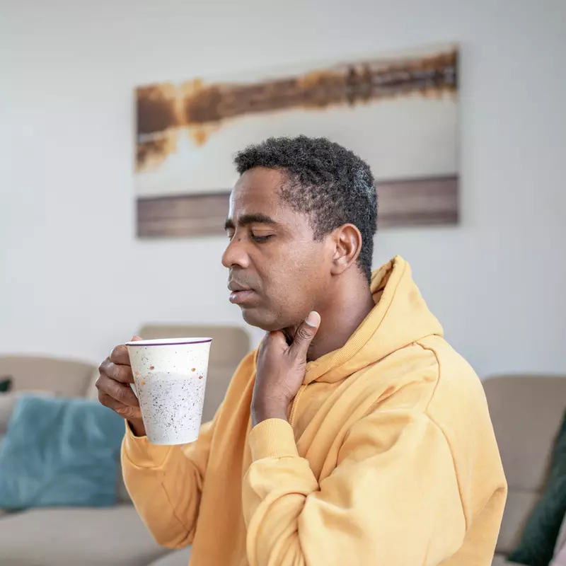 A man with a sore throat sips a cup of hot tea.