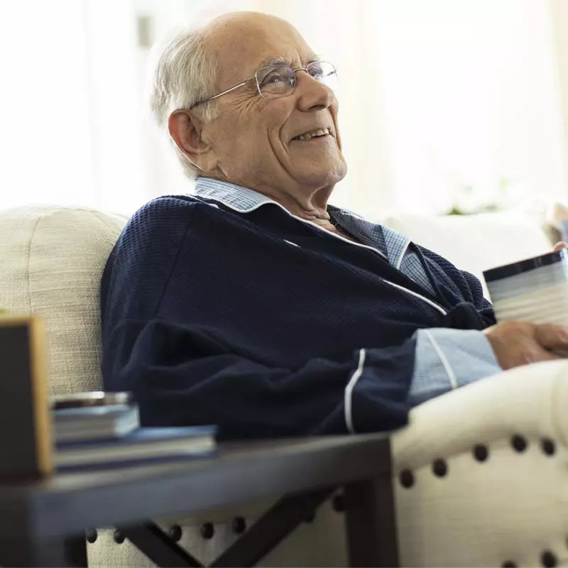 Elderly man sitting on couch drinking coffee.