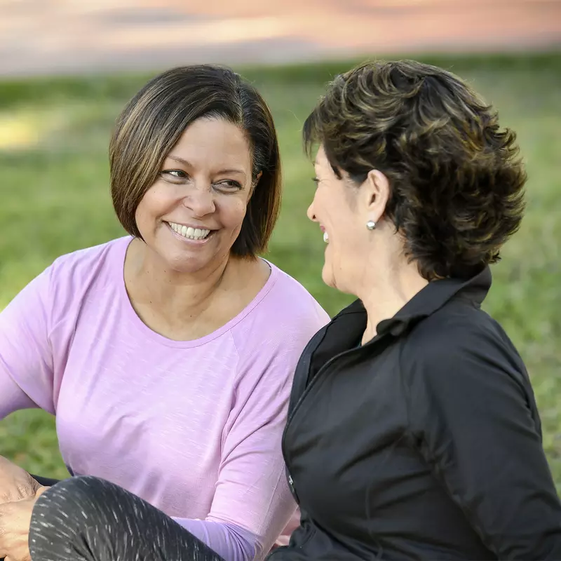 Two smiling women sitting outdoors talking