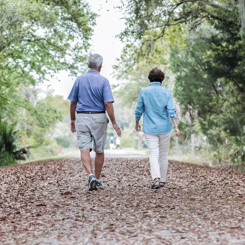 An elderly Caucasian couple takes an afternoon walk on a trail.