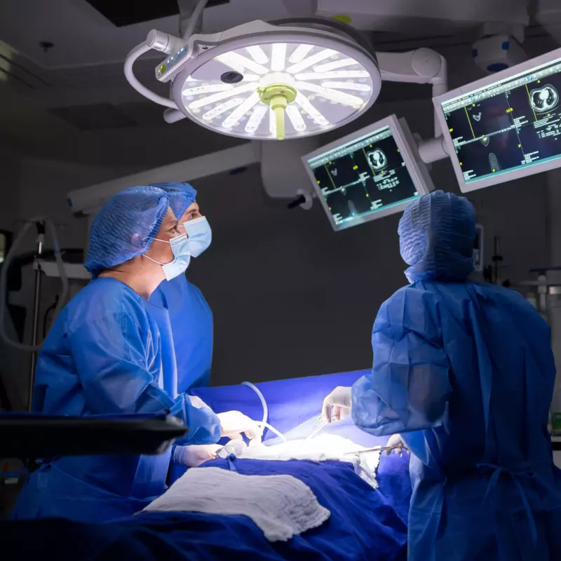 A surgical staff of three people performing a surgery in an operating room.