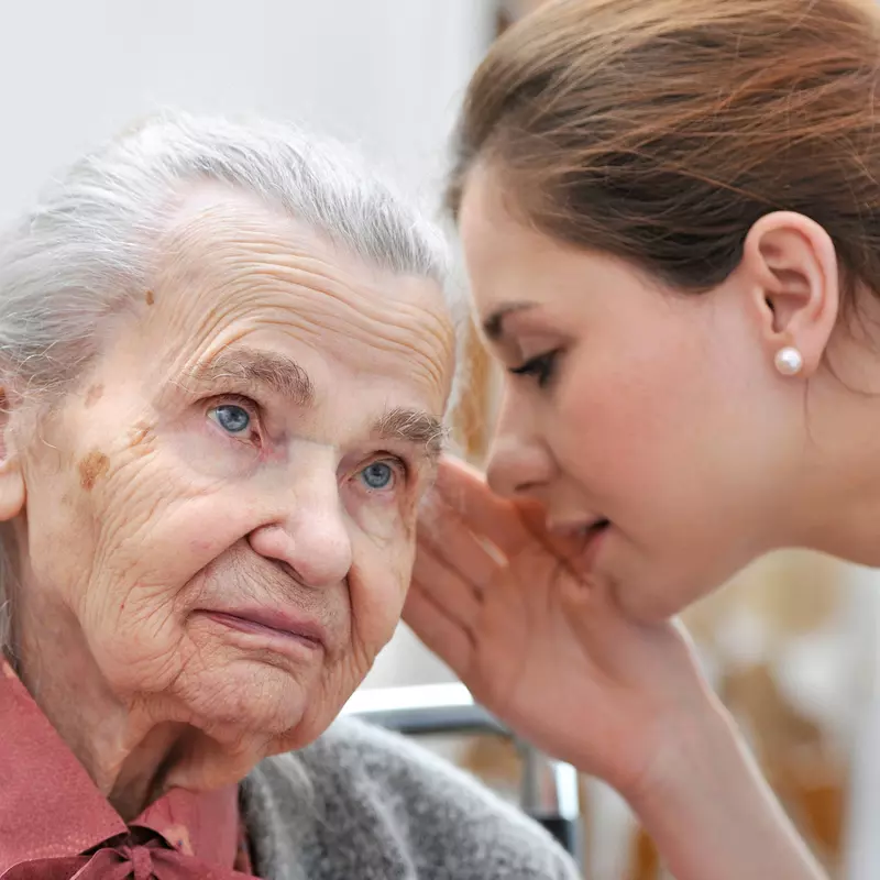 A younger woman whispers in an older woman's ear.