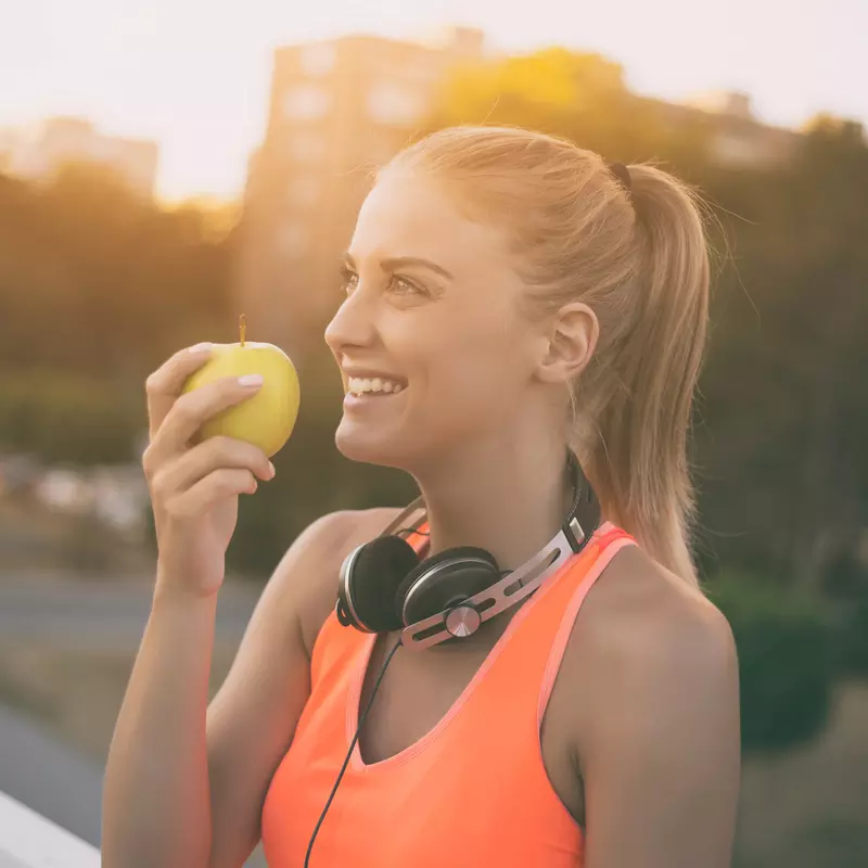 Woman wearing headphones and preparing to eat an apple
