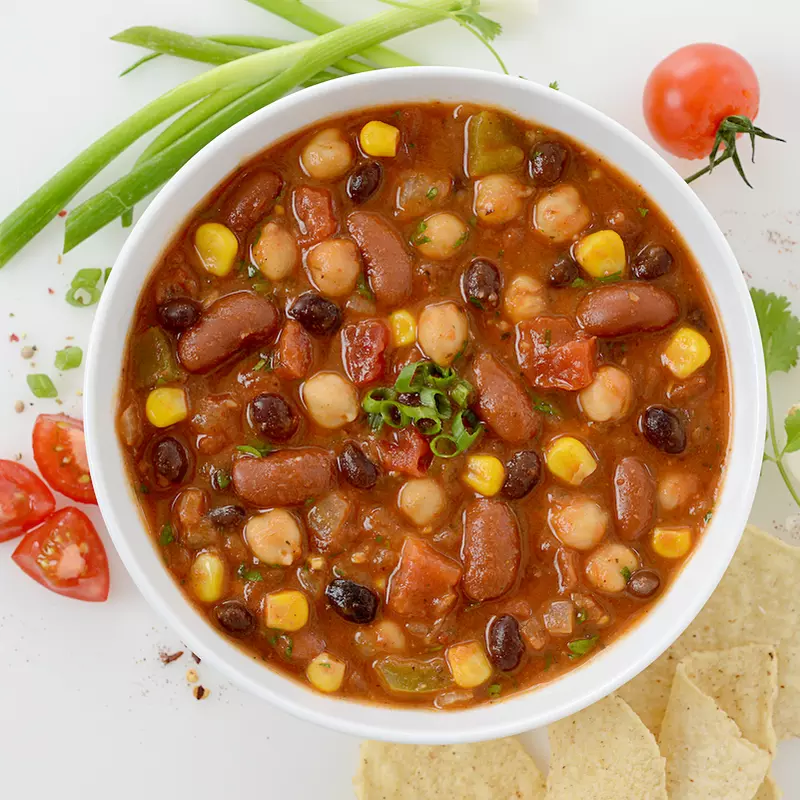 Bowl of three bean chili with corn and tomato and chive garnishes