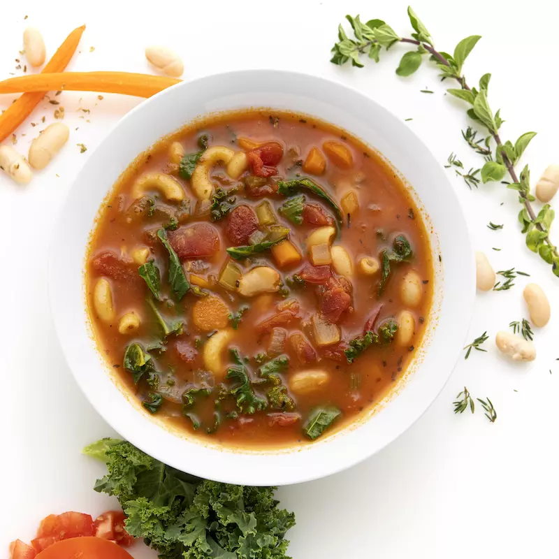 Bowl of white bean and kale soup with carrot and herb garnishes