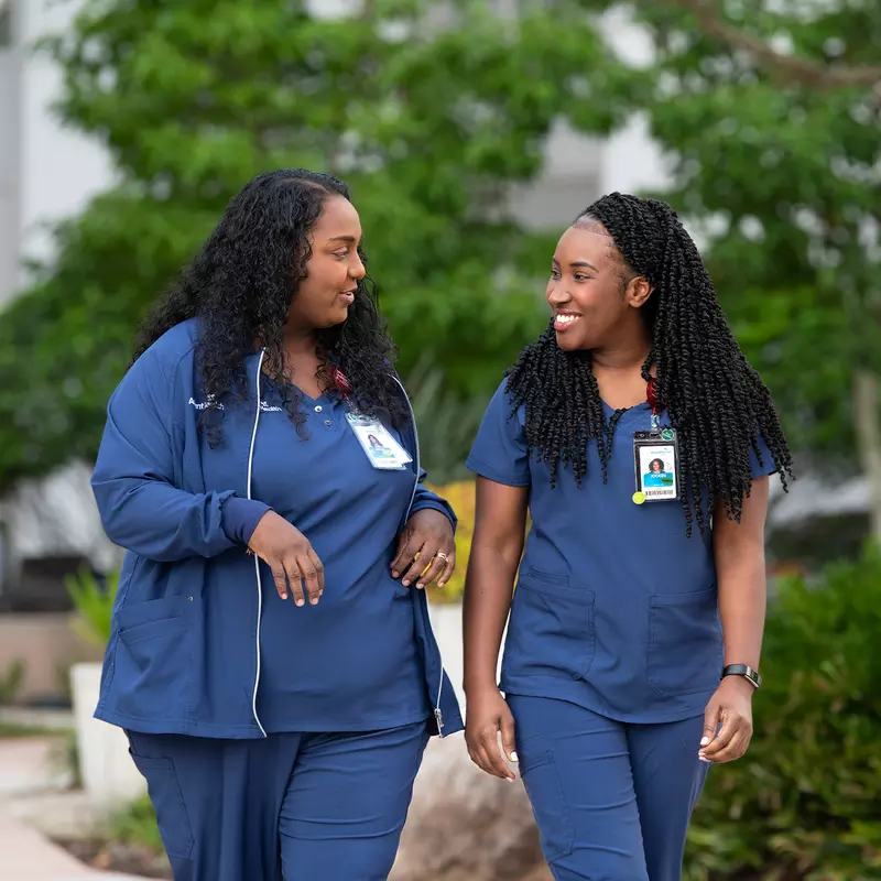 Two nurses walking outdoors and talking together.