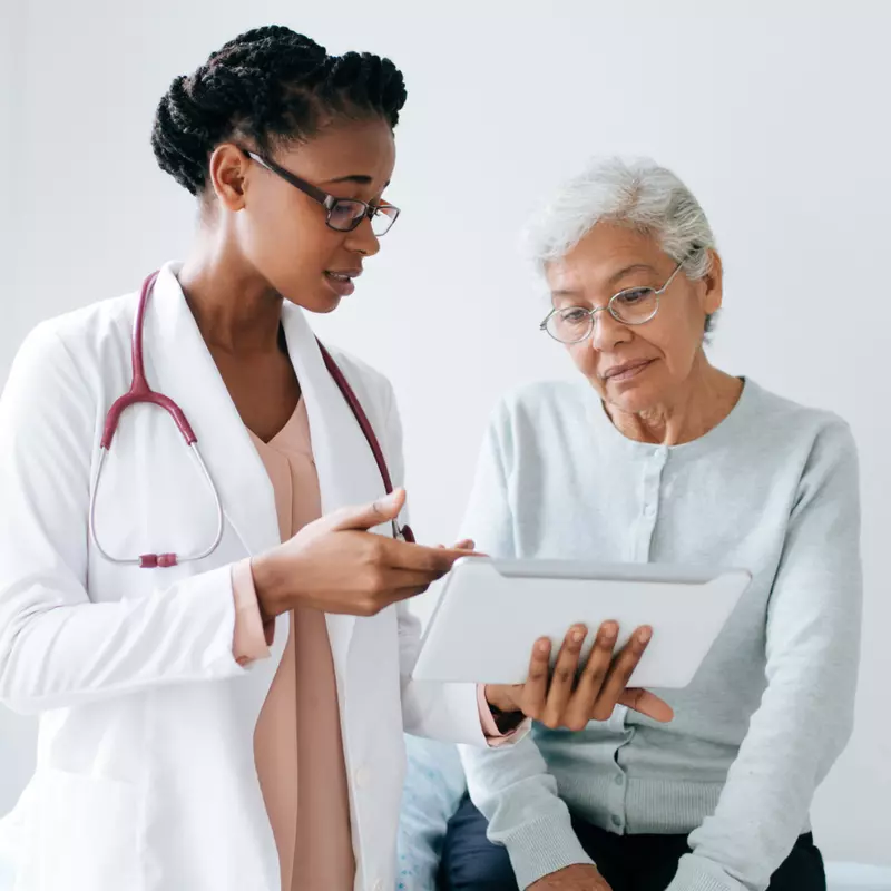 An older female patient and her physician look at a chart.