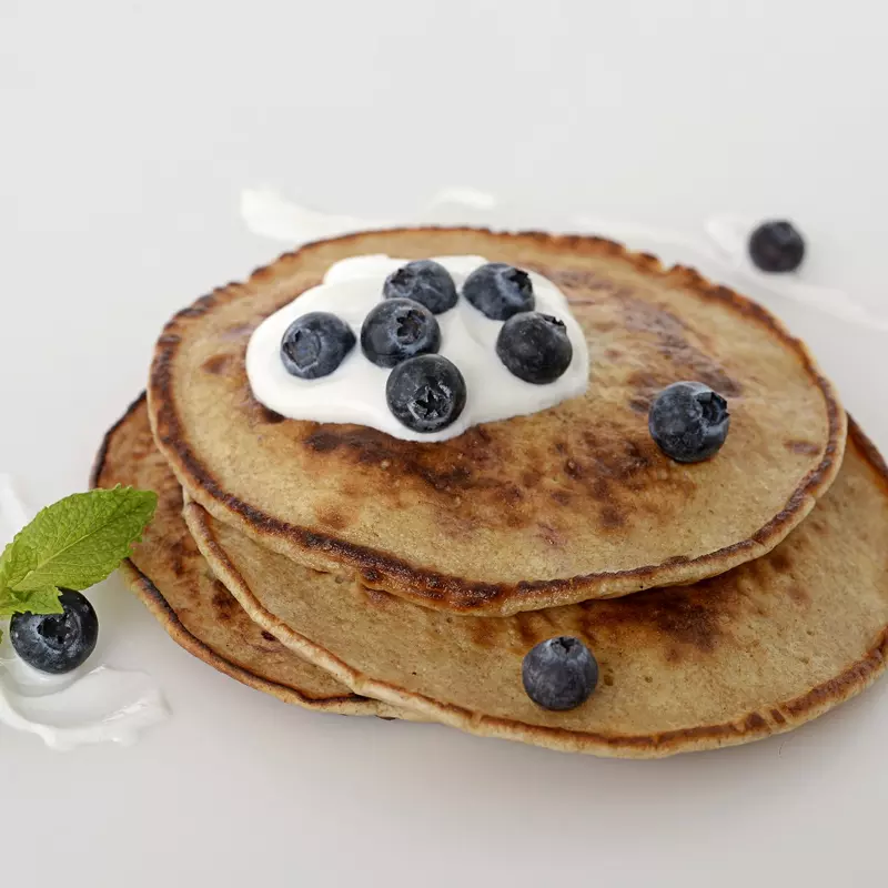 a stack of three homemade pancakes, topped with a dollop of Greek yogurt and fresh blueberries