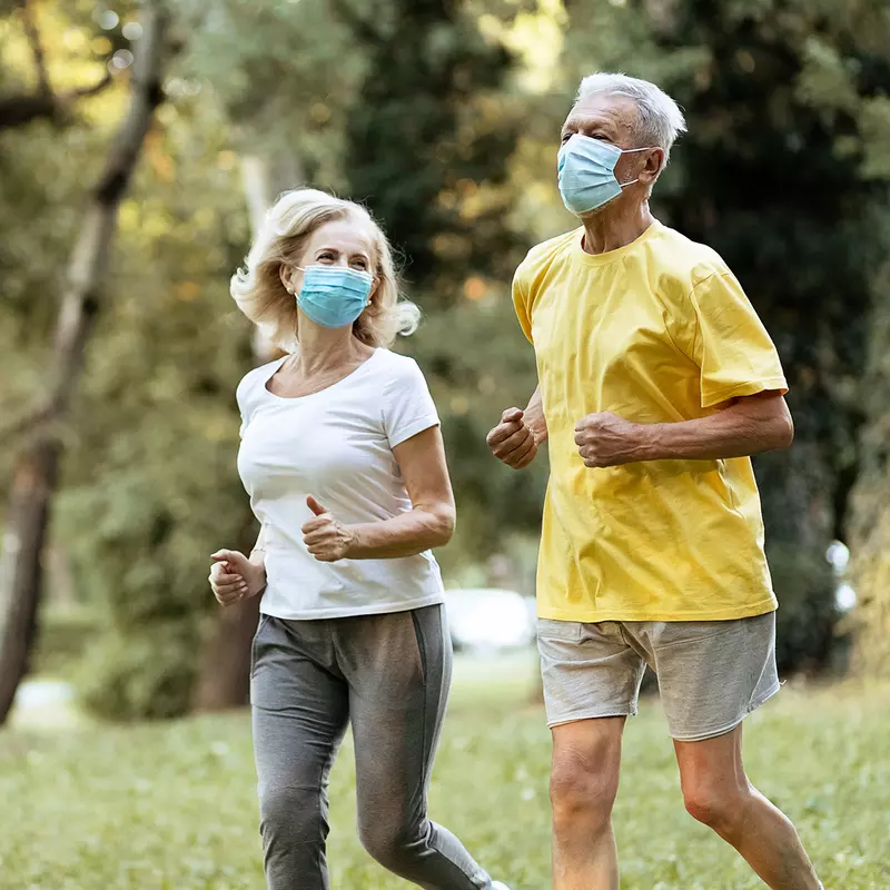 Older couple running outdoors while wearing masks.