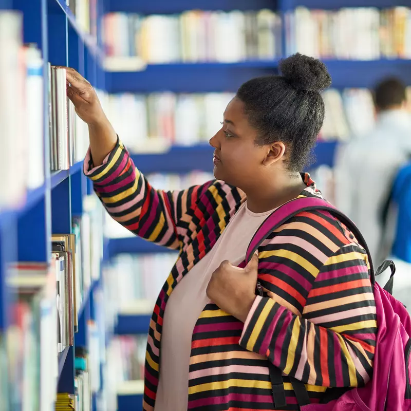 A woman of color selecting a book from the library