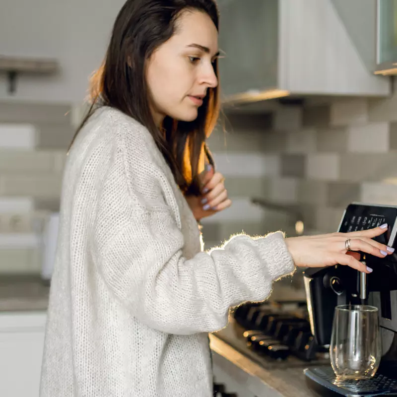 A woman in a kitchen using a coffee machine.