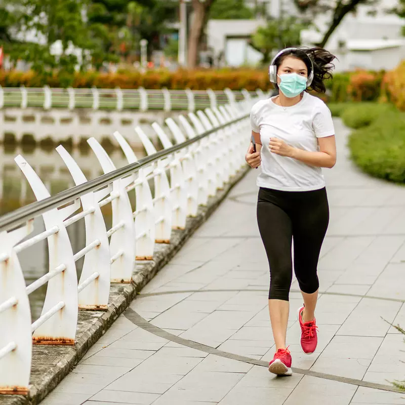 A woman exercising outside with a mask on.