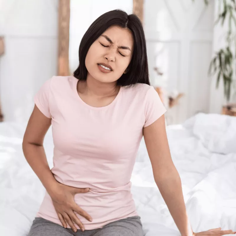 Woman sitting and holding lower abdomen in pain.