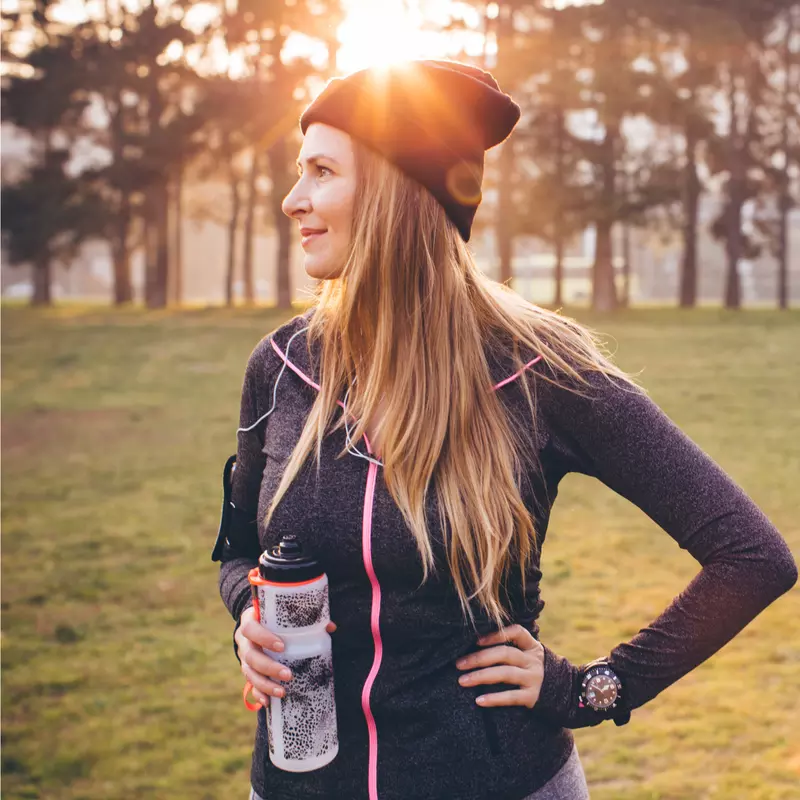 Woman wearing active wear and holding a water bottle in a park during winter.