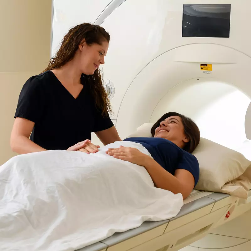 Woman inside medical imaging machine with a nurse standing next to her