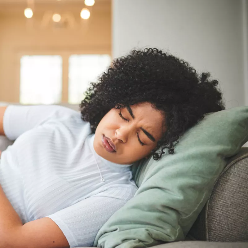 Woman laying on a couch at home holding her abdomen in pain.