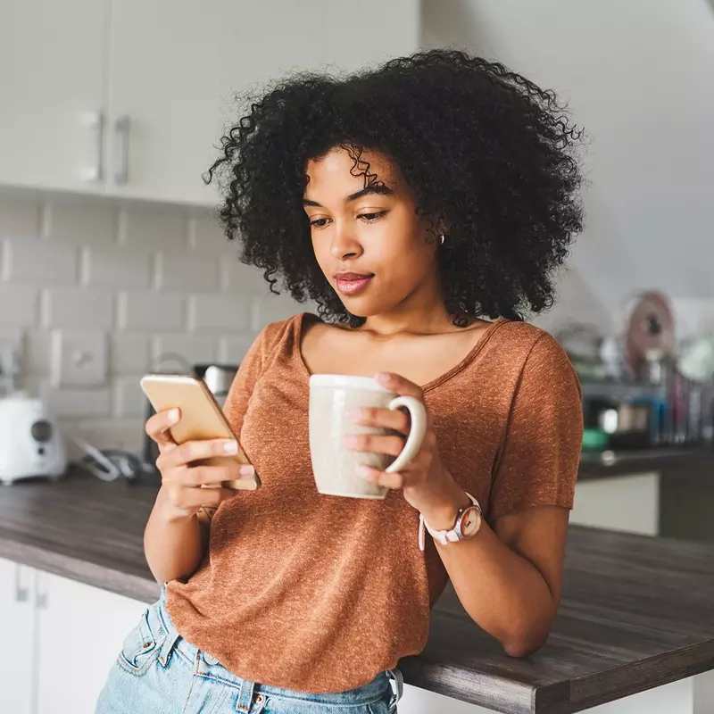 Woman during her morning routine: a cup of coffee while checking her phone.