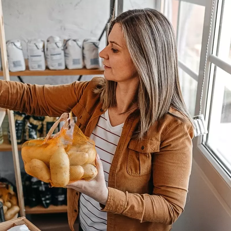 A woman holding a sack of potatoes and a can in a pantry.