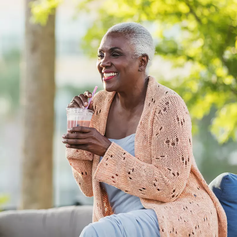 A Black Woman Enjoys a Smoothie on a Bench Outside