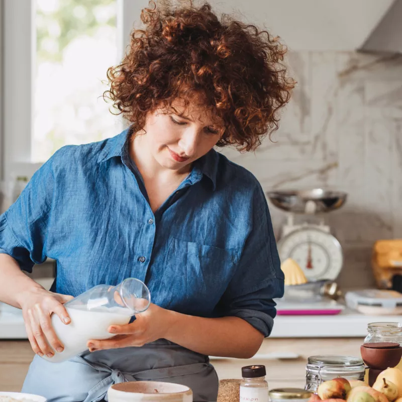 Woman pouring milk into a bowl while in a kitchen at home.