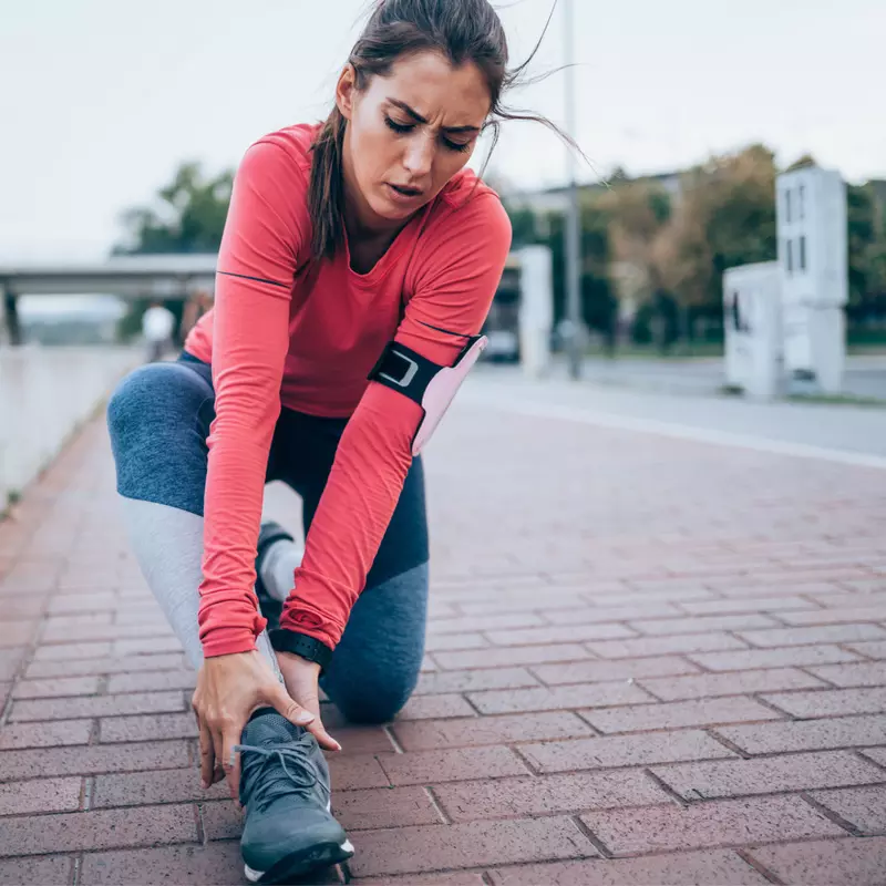 A woman runner holding her ankle while outdoors.