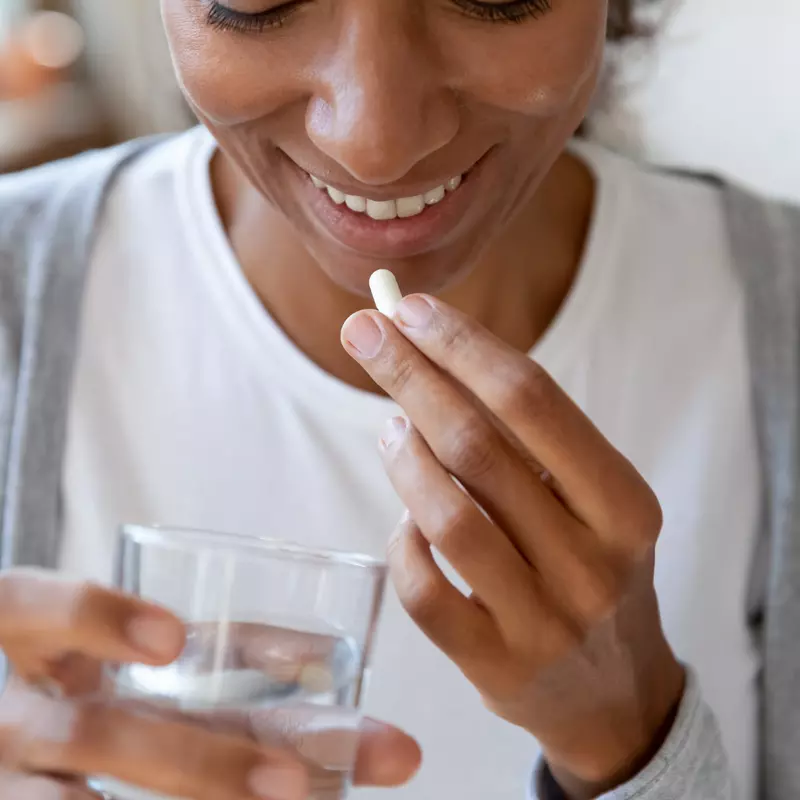 Woman taking a probiotic with a glass of water.