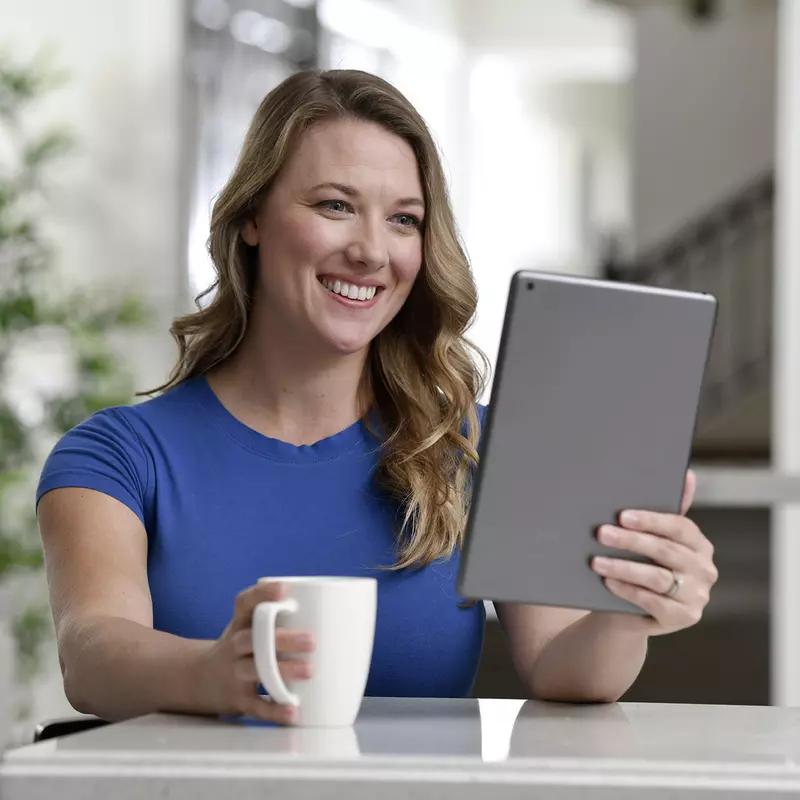 A smiling woman viewing a live event on a tablet.