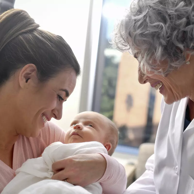 A mother holding her newborn baby with an older physician smiling at them