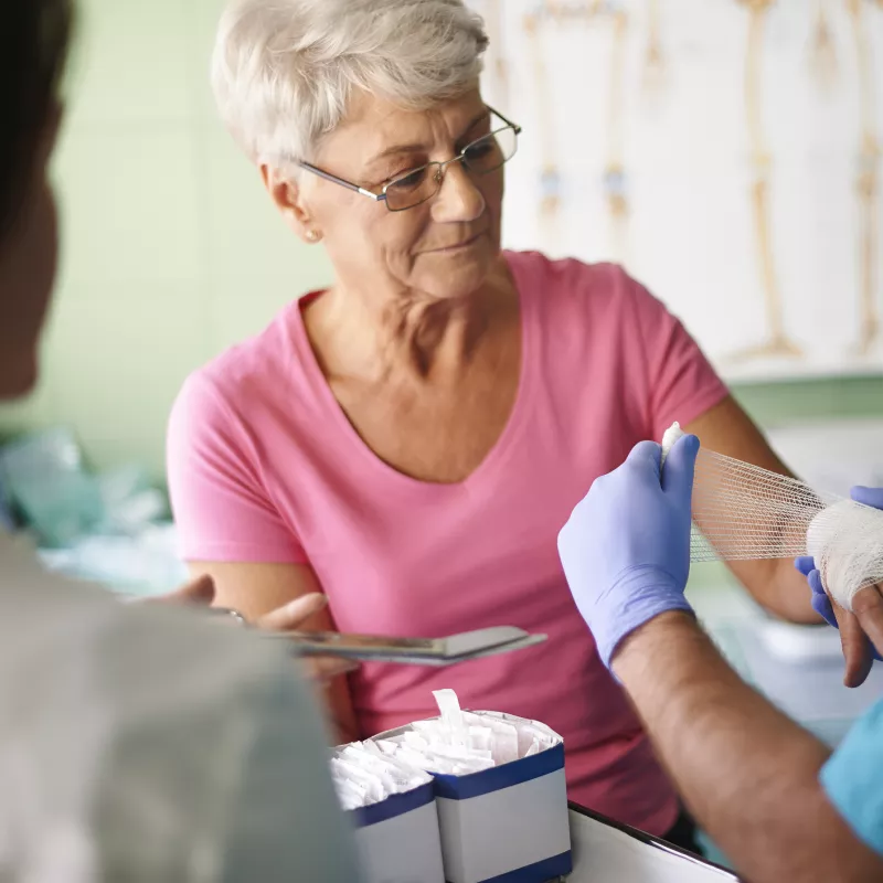 An older woman has her hand bandaged by a nurse