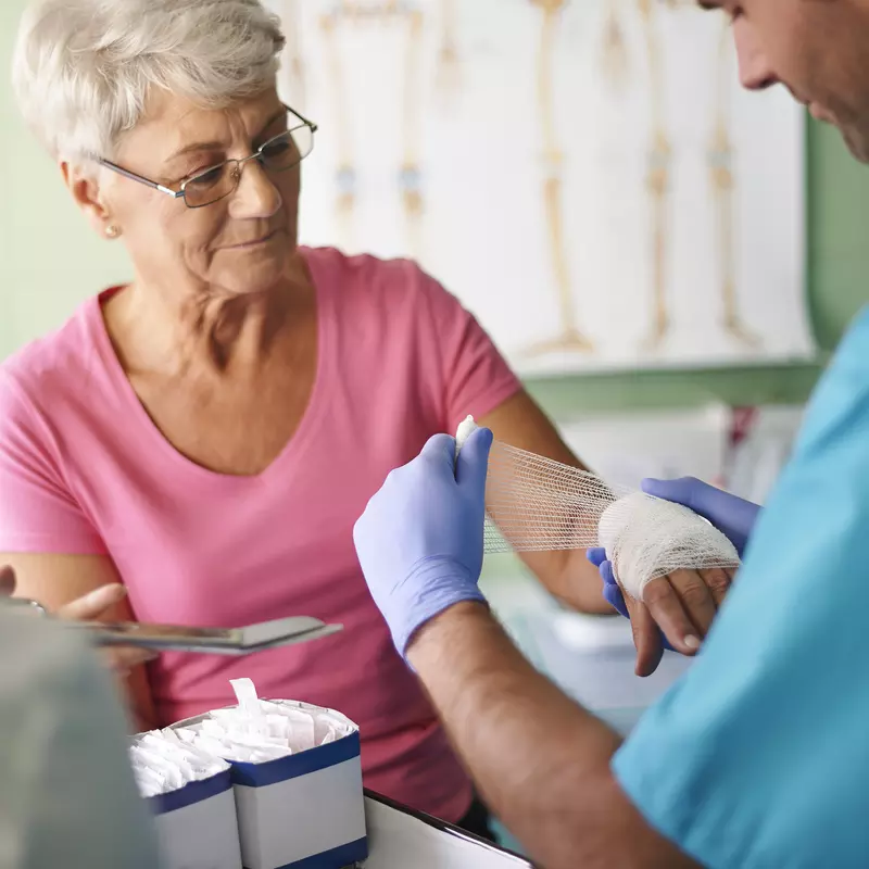 An older woman has her hand bandaged by a nurse