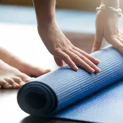 A woman unrolls a yoga mat.