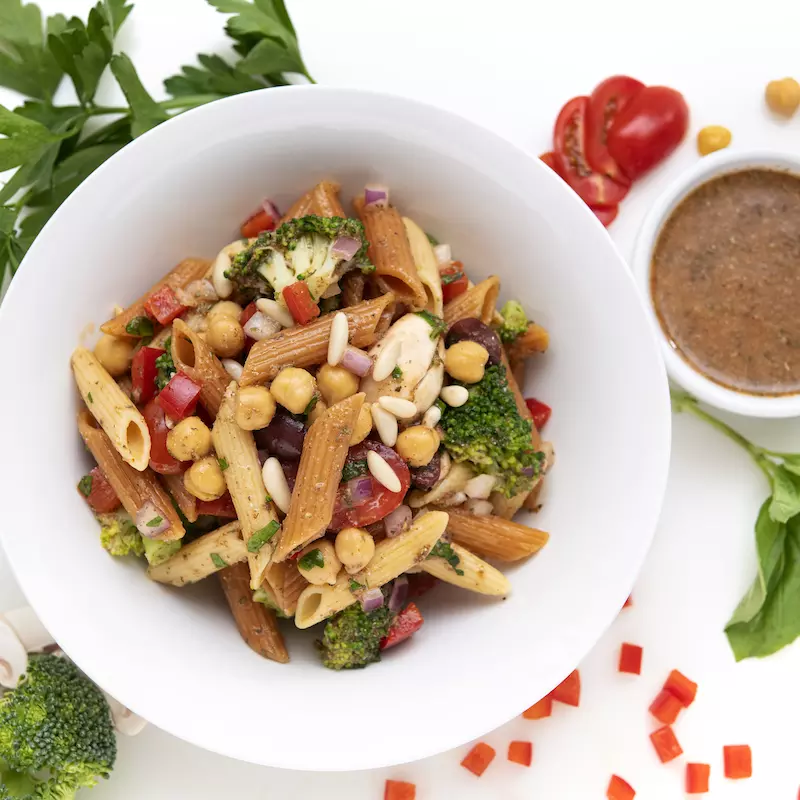 Bowl of pasta salad with brown sauce and leaf garnishes on the side