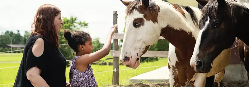 Daughter petting horse with mother behind her